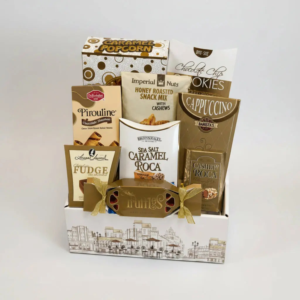 A gourmet gift basket filled with assorted chocolates, snacks, and treats, including Imperial Nuts Cashews, Siete Sal Caramel Roca, and various cookies, arranged in a white and gold cityscape-themed box.