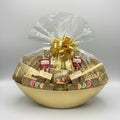 Gift basket with chocolates and snacks in a gold bowl on a dark surface.