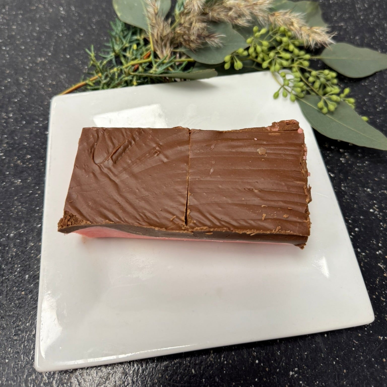 Chocolate bar on a white plate with greenery on a dark surface